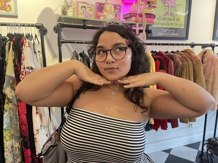 Ashley inside of a store, posing with her hands beneath her chin while she looks up to the left.